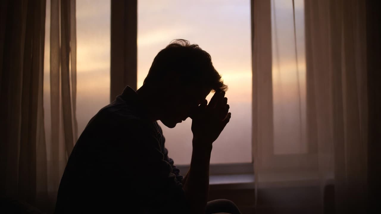 Persona sentada sola junto a una ventana al amanecer, con luz cálida entrando suavemente